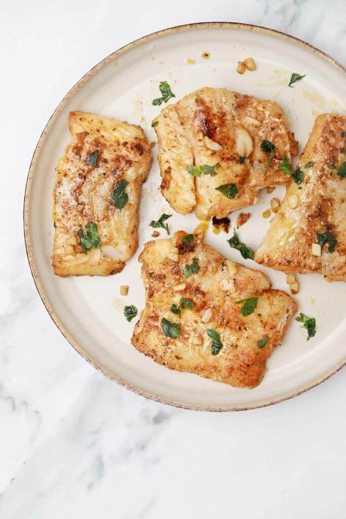 pan fried cod fillets on a plate garnished with parsley.