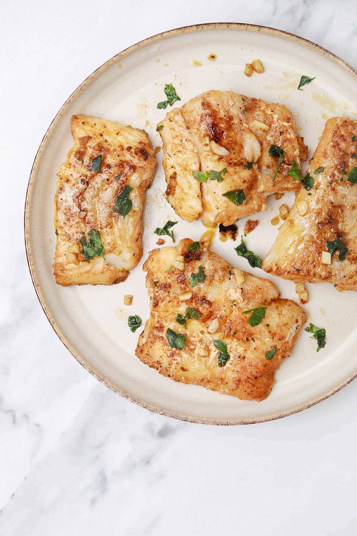 pan fried cod fillets on a plate garnished with parsley.