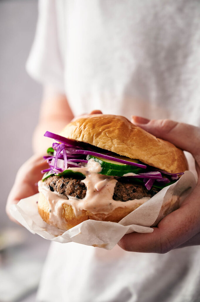 Holding an air fried bean burger that full of toppings and sauce.