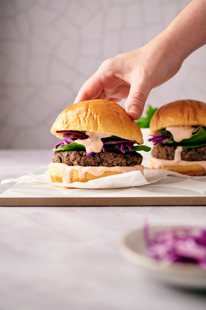 Someone placing a burger bun on a black bean burger.