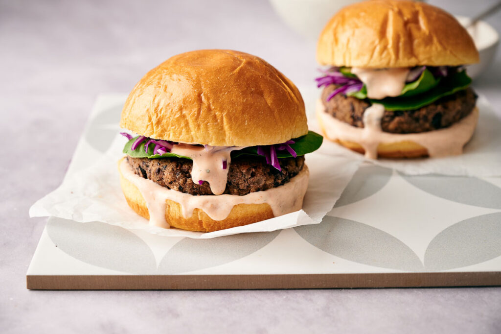 Two air fried black bean burgers in burger baps, with toppings and dressing, ready to eat.