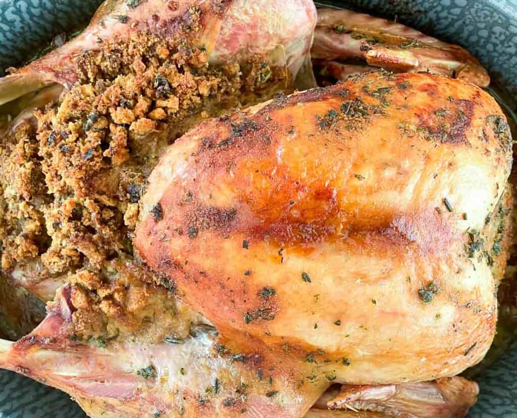 A roasted turkey in a bowl with seasonings.